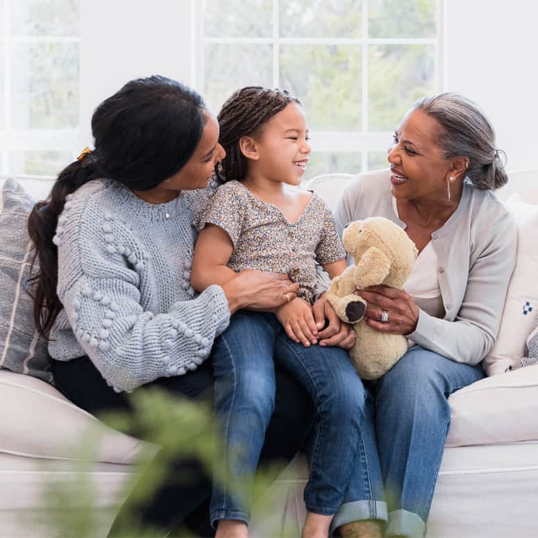 Young girl sits on a couch with her mother and grandmother.