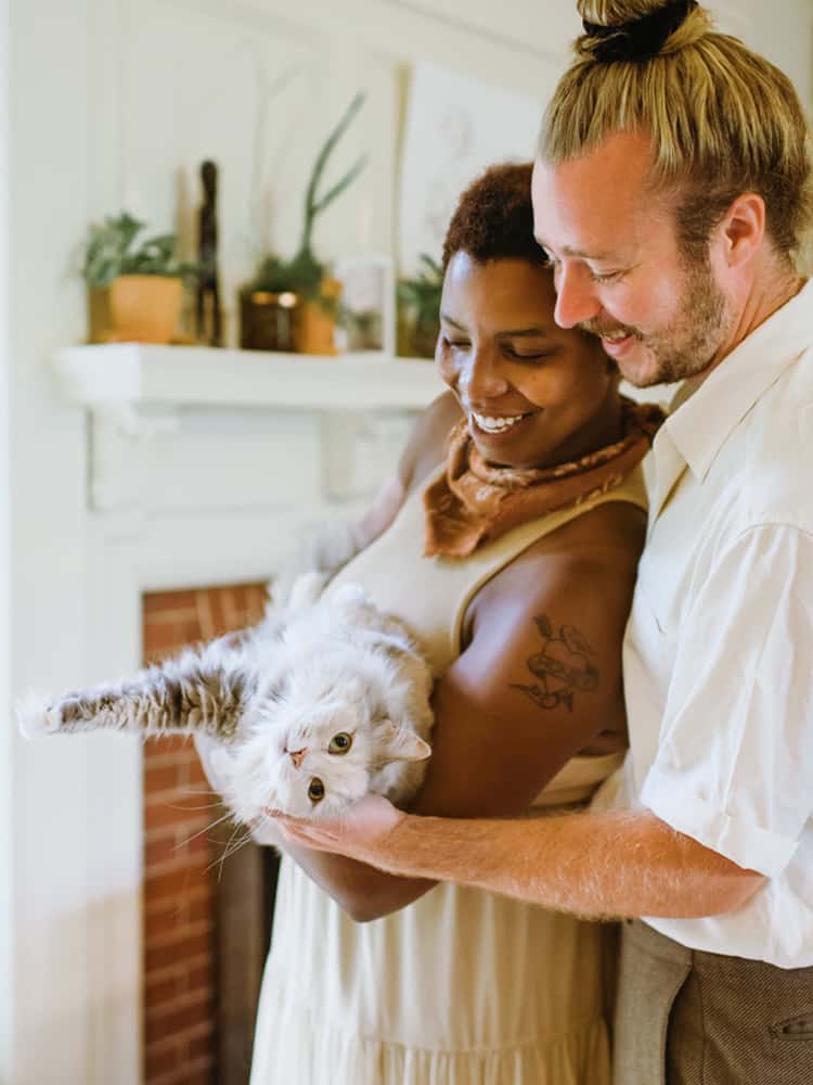 A woman and a man smile as they hold their cat.
