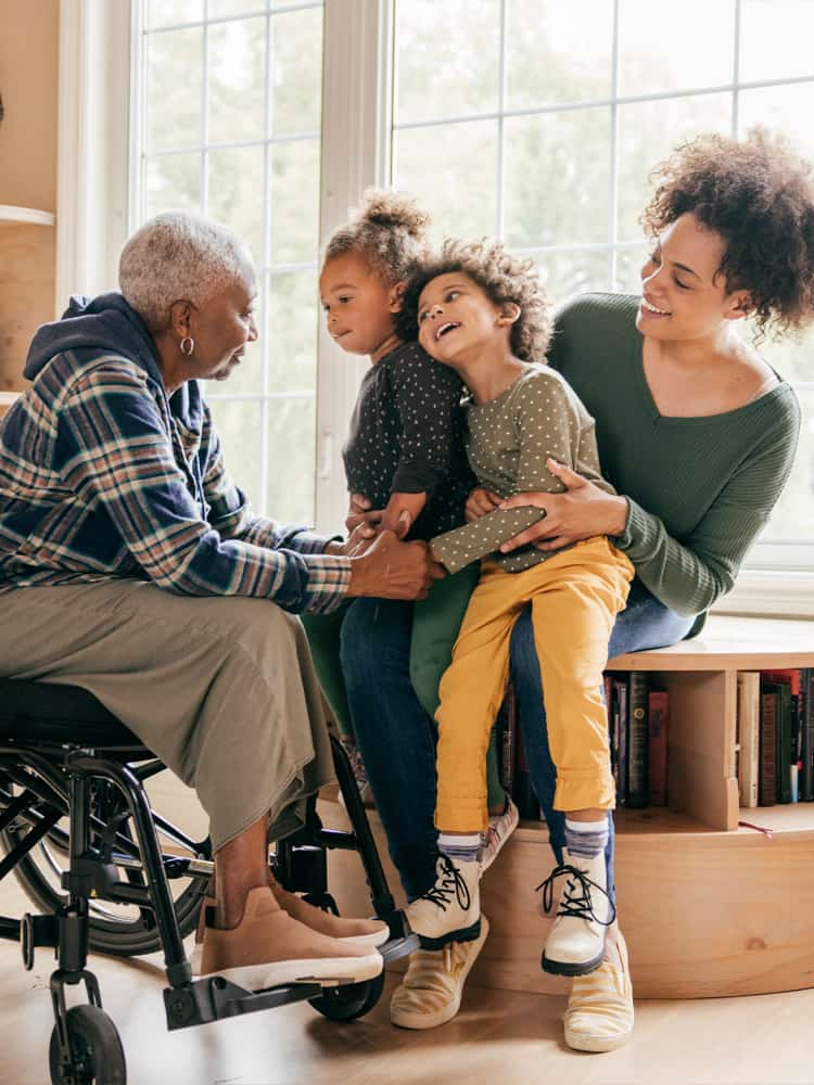 Two girls sit on their mother's lap while looking at their grandmother.