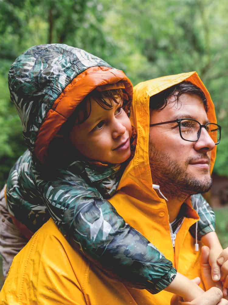A child rides on his father's back in the rain.