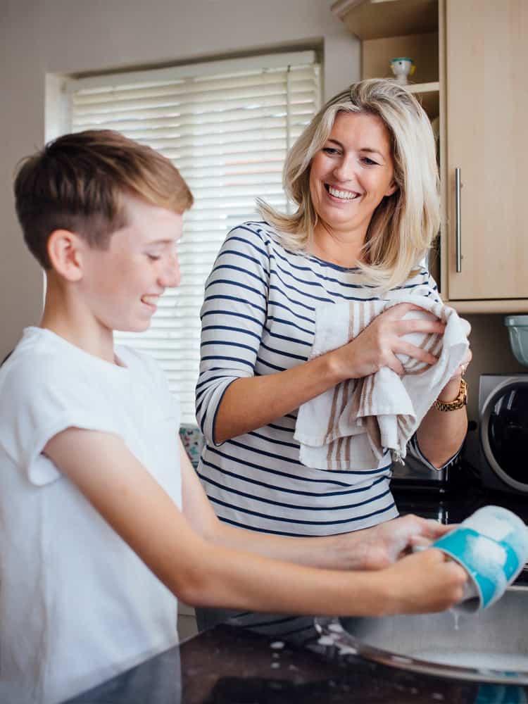 Woman and her teenage son laugh as they wash dishes.
